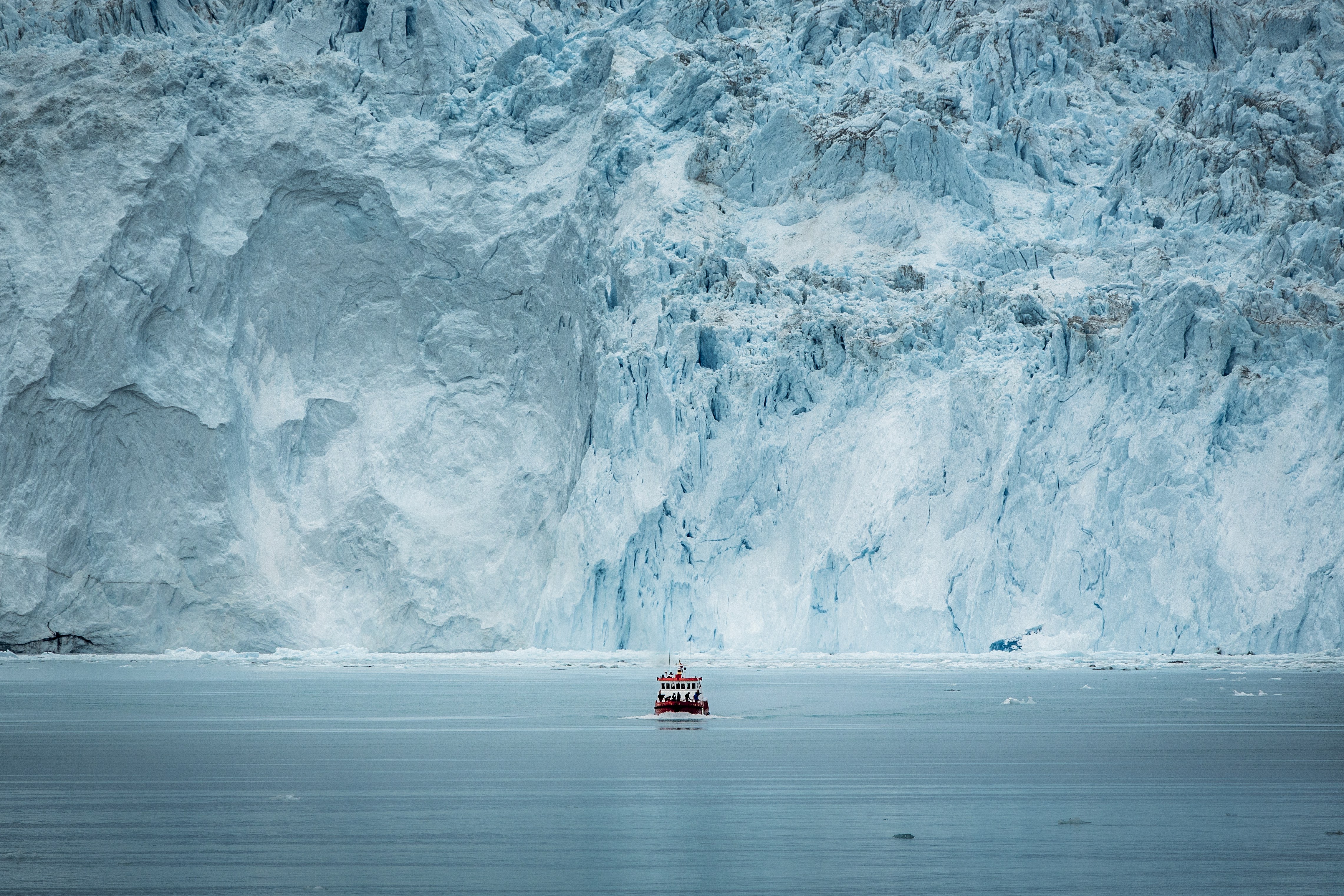 A Small Passenger Boat In Front Of The Huge Glacier Wall At The Eqi Glacier In Greenland